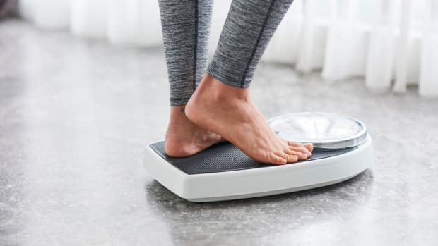 A woman wearing gray leggings standing on a bathroom scale
